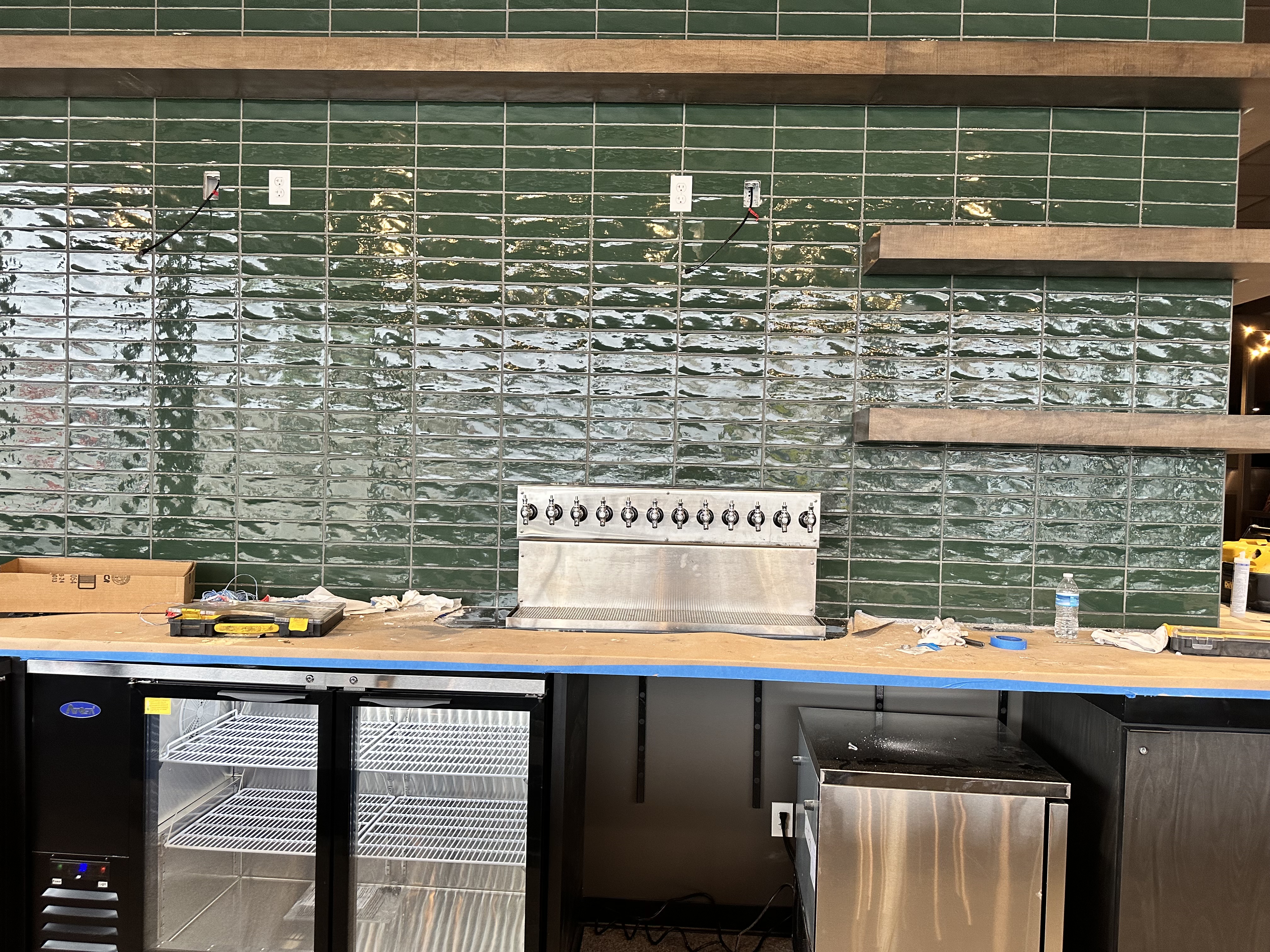 Bar under construction with green tile backsplash and 10-tap countertop tower